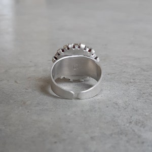 May include: Silver adjustable ring with a red and silver design. The ring has the letters "EC" stamped on the inside.