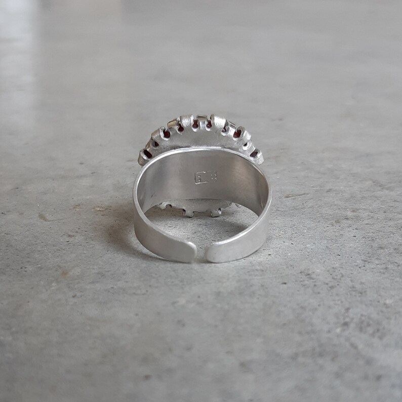May include: Silver adjustable ring with a red and silver design. The ring has the letters "EC" stamped on the inside.