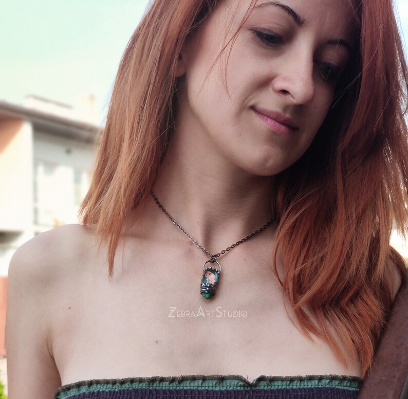 May include: A silver chain necklace with a pendant featuring a small, rectangular, green and pink glass piece with a floral design. The text "ZEBRA ART STUDIO" is visible below the pendant.