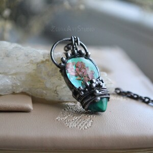 May include: A silver pendant necklace with a green and pink stone featuring a pressed flower design. The pendant is surrounded by silver wire and beads.