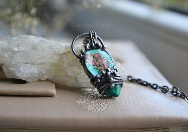 May include: A silver pendant necklace with a green and pink stone featuring a pressed flower design. The pendant is surrounded by silver wire and beads.
