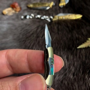 May include: A small, silver pocket knife with a mother-of-pearl handle. The knife is closed and has a silver chain attached to it.