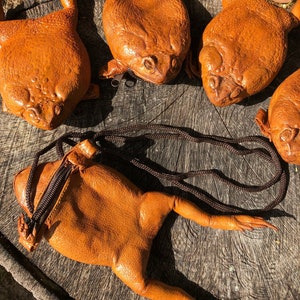 May include: Five brown leather frog purses with a zipper closure. The purses are arranged on a wooden surface.