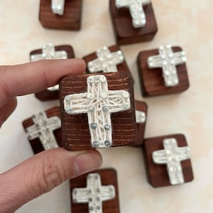 May include: Eight small wooden blocks with a white string cross design on each. The crosses are made with white string wrapped around nails and have silver glitter accents.