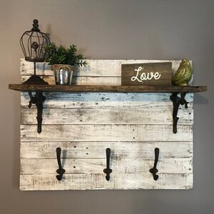 May include: Whitewashed wood shelf with three hooks and a brown wooden top. The shelf has a rustic look and is decorated with a birdcage, a potted plant, and a sign that says "Love".