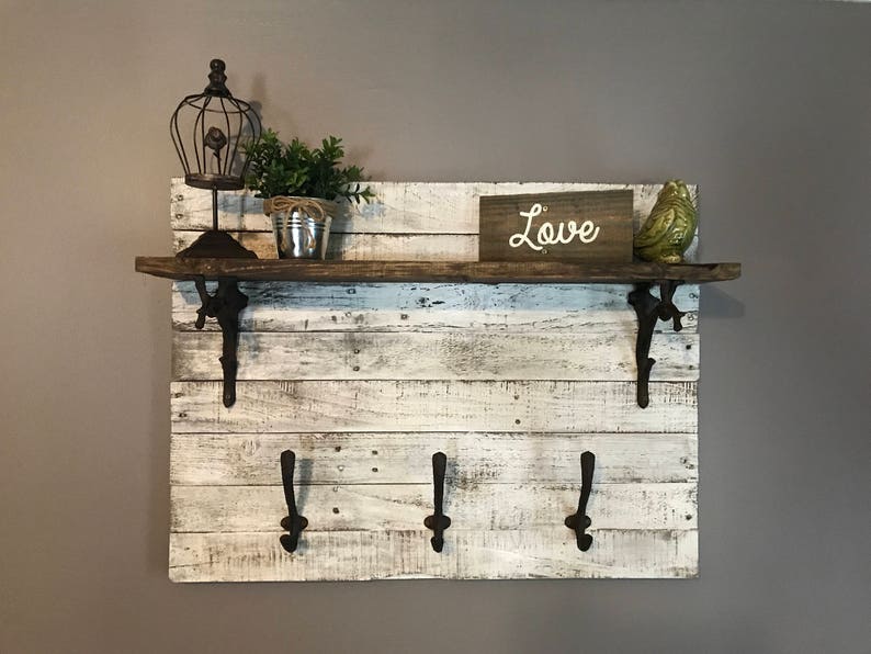 May include: Whitewashed wood shelf with three hooks and a brown wooden top. The shelf has a rustic look and is decorated with a birdcage, a potted plant, and a sign that says "Love".