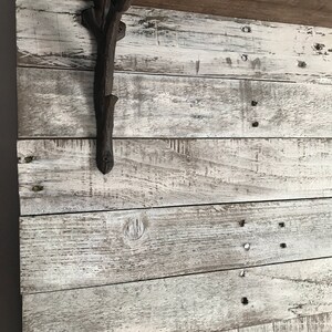 May include: A rustic, whitewashed wood wall with a dark brown metal branch-shaped hook attached to it. The hook is mounted on the top left side of the wall.