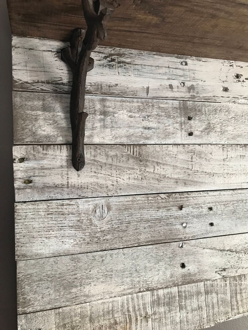 May include: A rustic, whitewashed wood wall with a dark brown metal branch-shaped hook attached to it. The hook is mounted on the top left side of the wall.