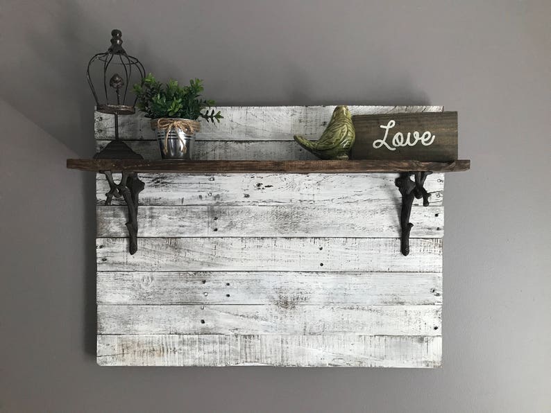 May include: Whitewashed wooden shelf with black metal brackets. The shelf is decorated with a small potted plant, a bird figurine, and a sign that says "Love".