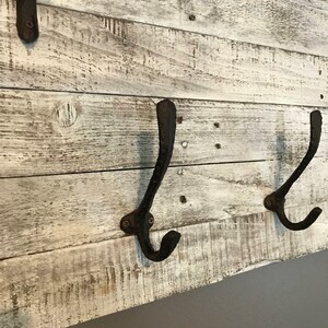 May include: Whitewashed wooden wall mounted coat rack with three black metal hooks.