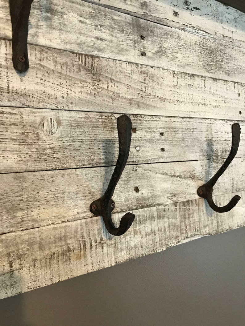 May include: Whitewashed wooden wall mounted coat rack with three black metal hooks.
