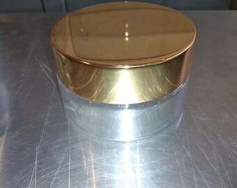 May include: A clear glass jar with a gold lid. The jar is empty and has a smooth, shiny surface.