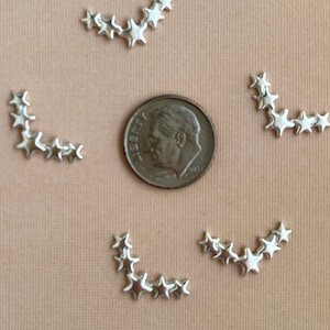May include: Four sets of silver star-shaped embellishments arranged in a curved line. Each set contains six stars and is about the size of a US dime.