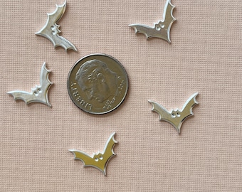 May include: Five silver-colored metal bat charms with a raised design. The bats are arranged around a US dime coin.