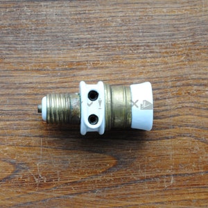 May include: A white ceramic light bulb socket with two brass terminals and a brass threaded end. The socket has a white plastic cap on the end.