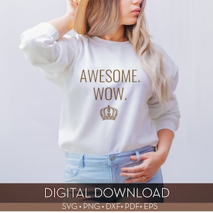 以下が含まれることがあります： 「AWESOME. WOW.」というテキストと金の王冠のグラフィックがプリントされた白いスウェットシャツ。モデルは青いジーンズを履いています。