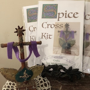 May include: A handmade wooden cross with a purple felt drape, adorned with dried herbs and a starburst at the top. Several "Spice Cross Kit" packages are in the background, with a decorative black metal piece in the foreground.