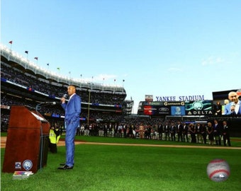 Puede incluir: Un hombre con un traje azul habla en un podio frente a una gran multitud en el Yankee Stadium. El marcador del estadio muestra las palabras "Yankee Stadium".