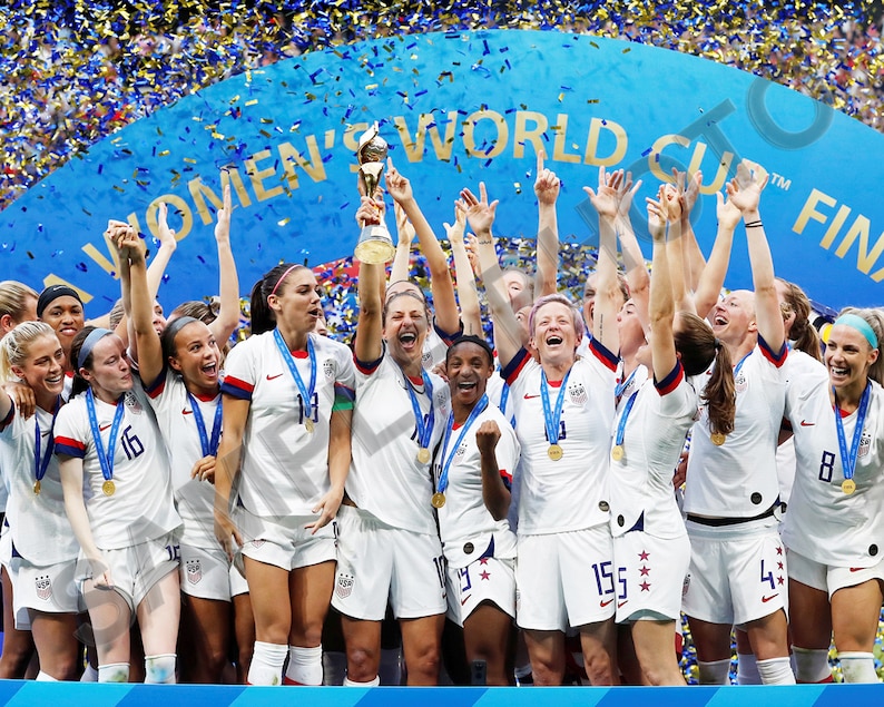 May include: A group of women in white and blue soccer uniforms holding up a trophy. They are all smiling and celebrating. The banner behind them reads "Women's World Cup Final".