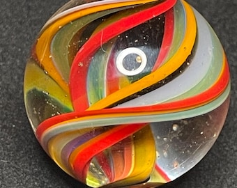 Pode incluir: Bola de gude de vidro transparente com faixas vibrantes e rodopiantes de cor. As faixas incluem vermelho, laranja, amarelo, roxo e verde, criando um design dinâmico e atraente. Um pequeno círculo branco é visível no centro.