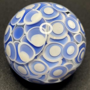 May include: A glass sphere with a pattern of blue and white concentric circles. The sphere is a decorative object, with a glossy finish and a complex, layered design. The blue and white colors create a striking contrast.