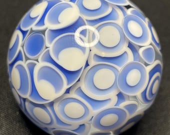 May include: A glass sphere with a pattern of blue and white concentric circles. The sphere is a decorative object, with a glossy finish and a complex, layered design. The blue and white colors create a striking contrast.