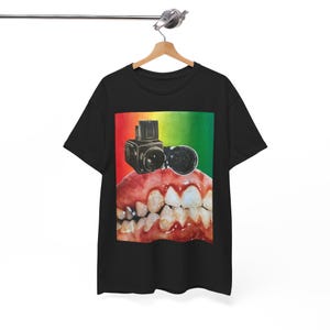 May include: Black t-shirt featuring a graphic design. The design includes a close-up of teeth with a camera and a lens superimposed on the gums. The background transitions from red to yellow to green.