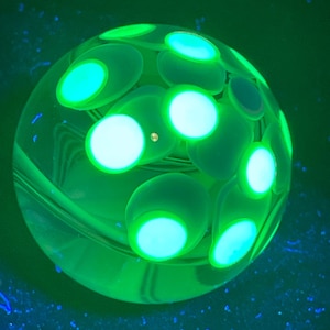 May include: A glowing green glass sphere with multiple light green, oval-shaped accents. The sphere has a clear, transparent base with a swirling pattern. The accents are illuminated with a bright, neon green light, creating a striking visual effect.