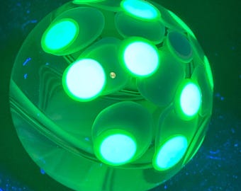 May include: A glowing green glass sphere with multiple light green, oval-shaped accents. The sphere has a clear, transparent base with a swirling pattern. The accents are illuminated with a bright, neon green light, creating a striking visual effect.