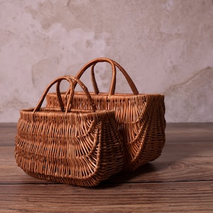 May include: Two brown wicker baskets with handles, one slightly larger than the other, sitting on a wooden surface.