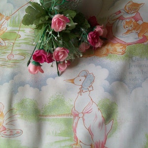 May include: A white fabric with a light blue background featuring a duck, a mouse, and a rabbit. The fabric has a floral pattern with pink and white flowers. The text "Quack quack said Jemima Puddle-duck with her head on side" is printed on the fabric.