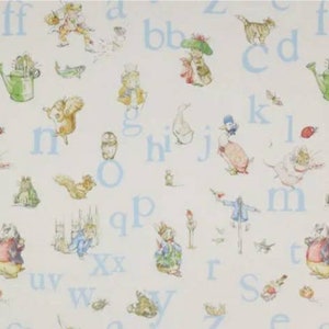 May include: A white fabric with a blue alphabet pattern and illustrations of animals and characters from the Peter Rabbit stories. The letters are in a light blue font and the illustrations are in a vintage style.