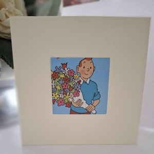 Peut inclure: Une carte de vœux avec une image de dessin animé d'une personne tenant un bouquet de fleurs colorées. La personne porte un pull bleu et a les cheveux roux.