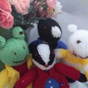 May include: Four knitted stuffed animals: a green frog, a black and white badger, a white rabbit, and a black bird. The animals are wearing colorful knitted clothing.