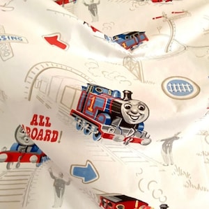 May include: White fabric with a repeating pattern of Thomas the Tank Engine and other train characters. The fabric features the words "All Aboard!" and "Crossing" in a cartoon font.