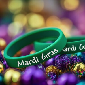 May include: Two green rubber bracelets with the text "Mardi Gras" in white lettering. The bracelets are lying on a bed of purple, gold, and green beads.