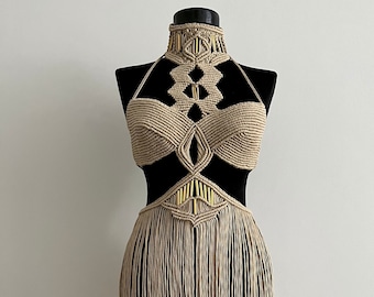 May include: A beige macrame halter top with a geometric design and fringe. The top is made of natural fibers and has a bohemian style.