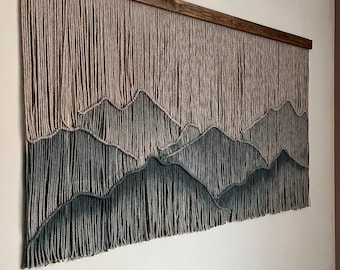 May include: A wall hanging with a mountain range design made with yarn. The yarn is a light brown color at the top and fades to a dark green at the bottom. The hanging is framed with a dark wood frame.