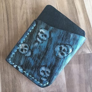 Könnte beinhalten: Ein handgefertigter Kartenhalter aus Leder in Blau- und Schwarztönen mit einem Totenkopfmuster. Der Kartenhalter ist mit hellblauem Faden genäht und enthält eine schwarze Karte.