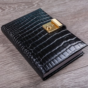 May include: A black leather-bound journal with a gold lock and keyhole. The journal has a crocodile-embossed pattern.