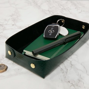 May include: A green leather tray with gold accents holds a notebook, pen, and car key.
