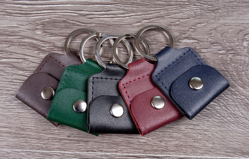 May include: Five leather keychains with metal rings. The keychains are in different colors: brown, green, black, burgundy, and blue.