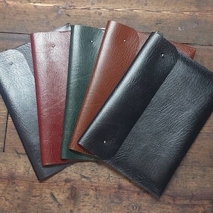 May include: Five leather folders in different colors, including black, brown, green, and red. The folders are arranged in a fan shape, with the black folder on top.