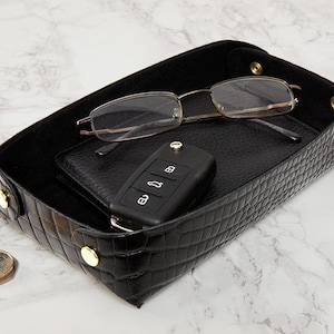 May include: Black leather tray with a crocodile pattern, featuring a pair of glasses, a car key, and a black leather wallet.