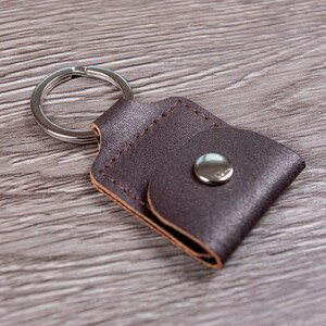 May include: A brown leather keychain with a silver ring and a small flap with a silver button.