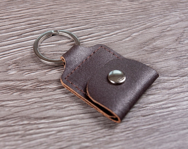 May include: A brown leather keychain with a silver ring and a small flap with a silver button.
