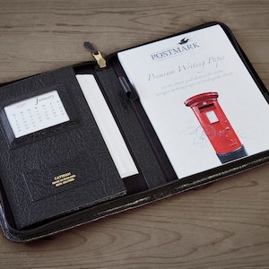 May include: Black leather zippered folder with a calendar insert and a stack of premium writing paper inside. The paper has a red postbox illustration and the text "Postmark Premium Writing Paper 50 sheets pad of smooth white 100gsm writing paper & lined guide sheet"