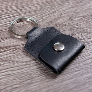 May include: A black leather key chain with a silver ring and a snap closure.