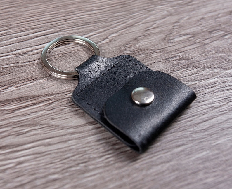 May include: A black leather key chain with a silver ring and a snap closure.