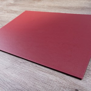 May include: A burgundy leather desk mat. The mat is flat and rectangular with stitched edges.